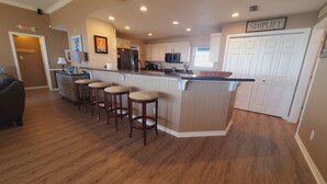 A modern kitchen with a central island, bar stools, white cabinetry, and a microwave.