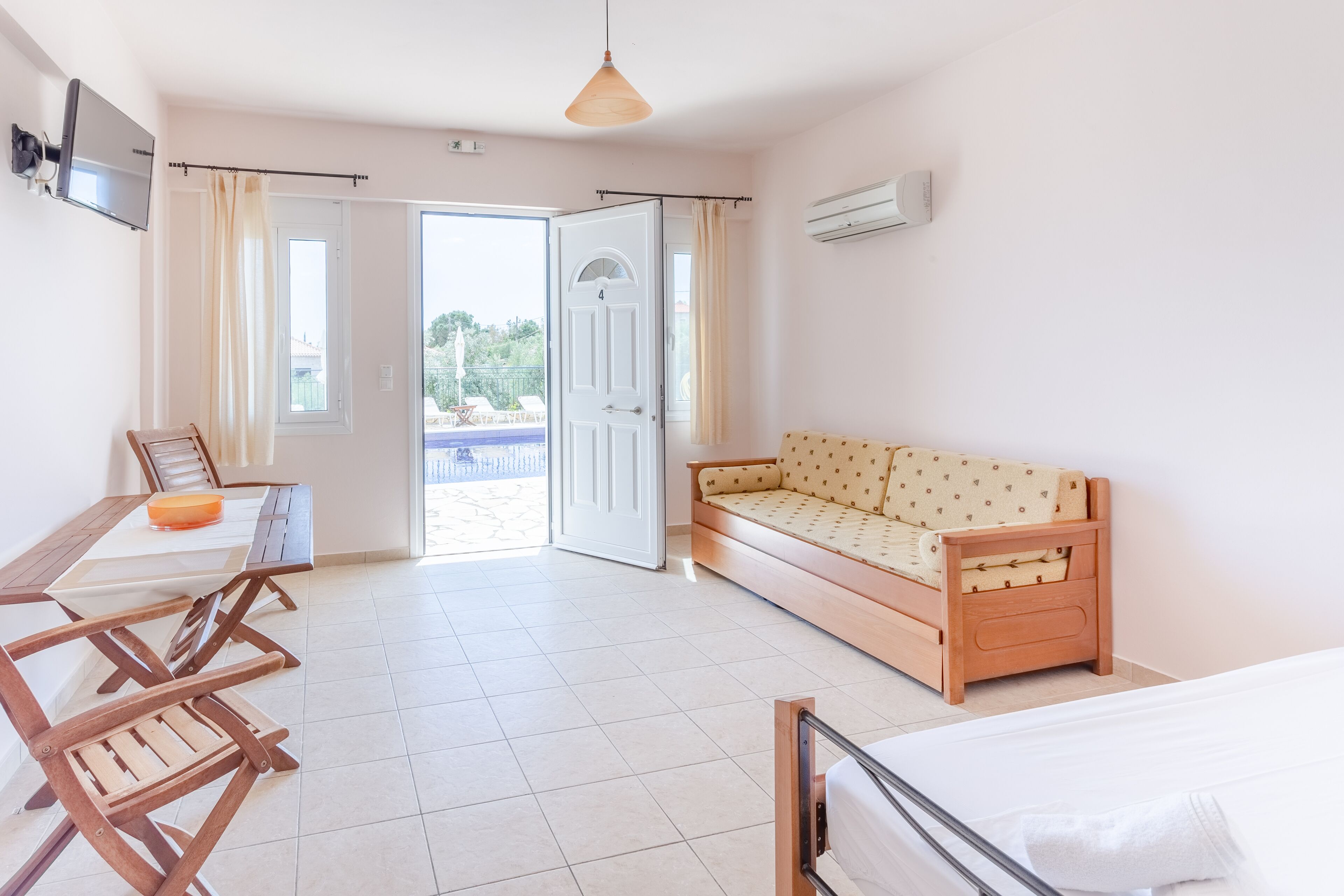 Una habitación con una cama, un sofá, una mesa de comedor con sillas, un televisor y una puerta que da a un espacio exterior.