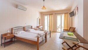 Habitación de hotel con dos camas individuales, un escritorio con silla, televisor montado en la pared y un ventanal con cortinas.
