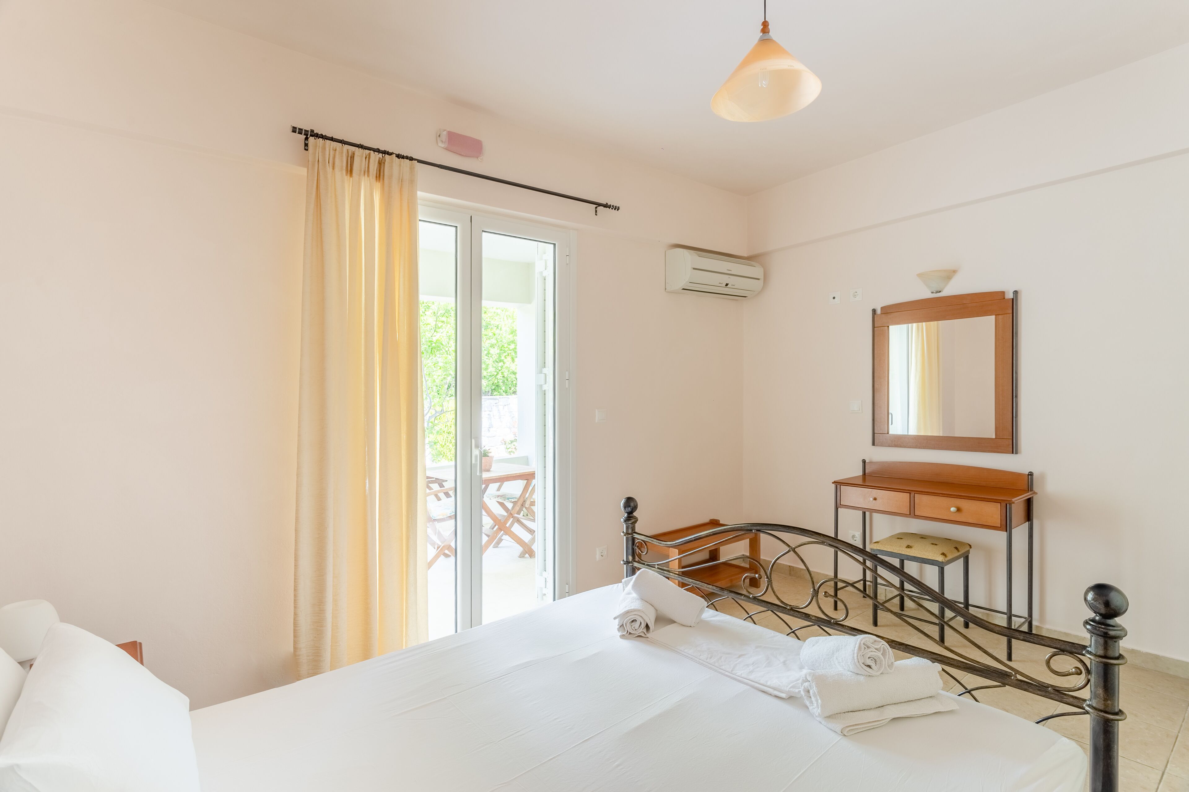 A hotel room with a bed, a desk, a chair, a mirror, and a sliding glass door leading to an outdoor area.