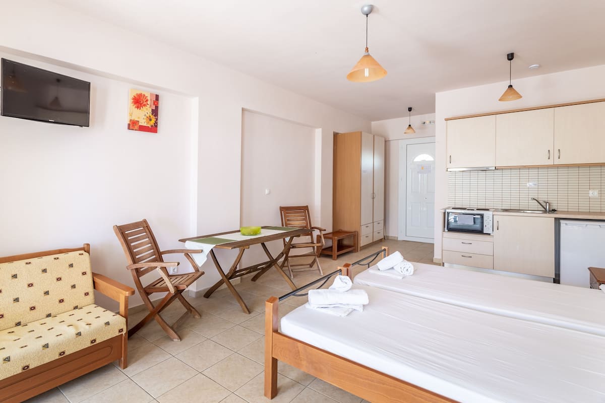 Habitació d'hotel moderna amb un llit, un sofà, una taula de dinar amb cadires, zona de cuina amb microones i televisió penjada a la paret.