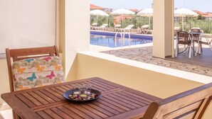 Una mesa de madera con un plato de aperitivos y vasos, con vistas a una zona de piscina con sillones y sombrillas.