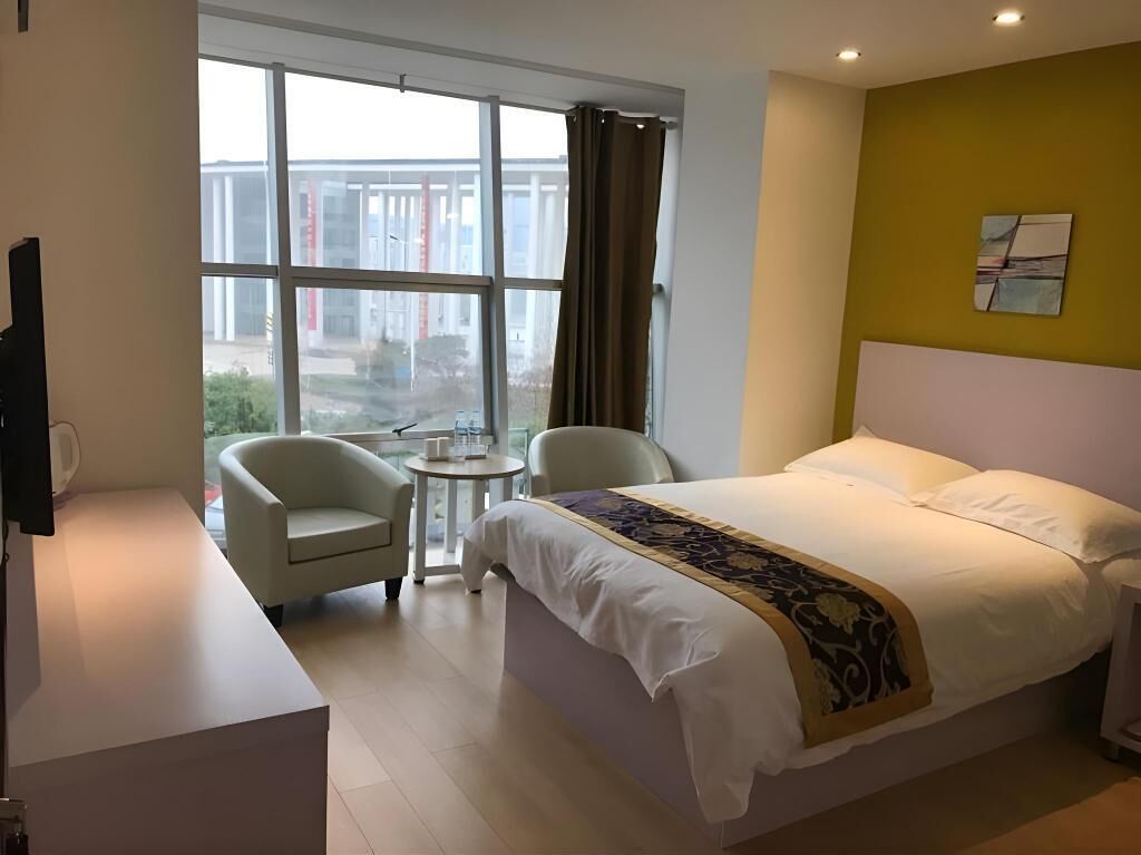Habitación de hotel con cama, escritorio, silla, mesita y ventana con cortinas.