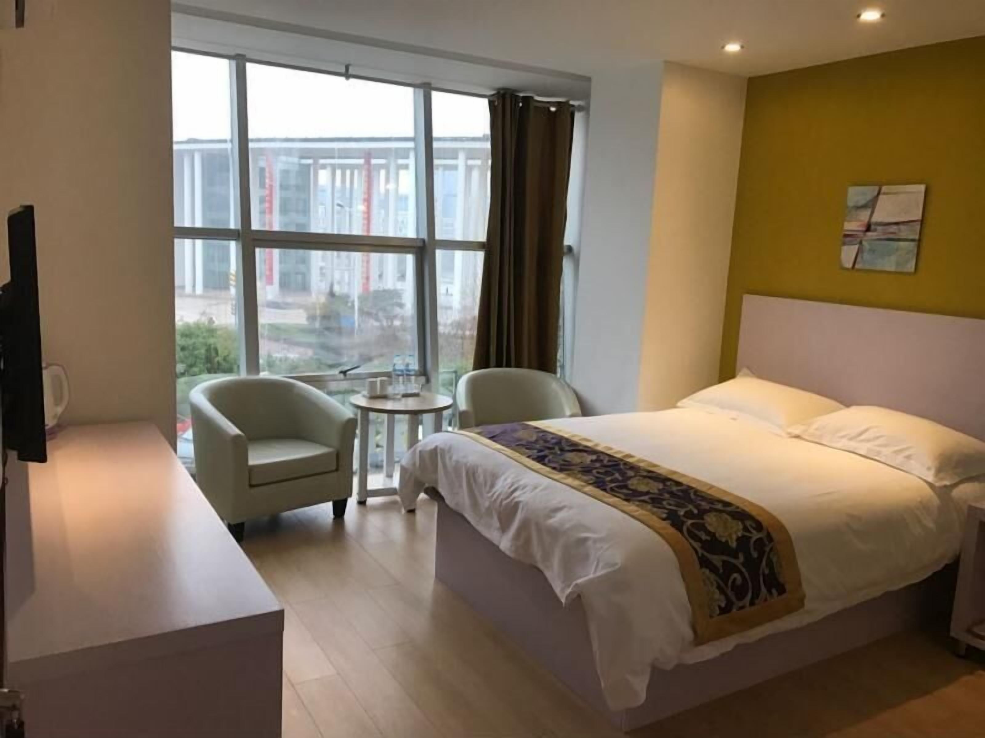 Ein Hotelzimmer mit Bett, zwei Stühlen, einem kleinen Tisch und einem großen Fenster.