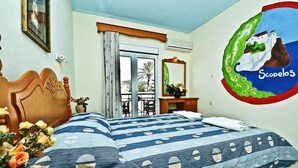 A hotel room with a bed, a wooden headboard, a window with curtains, a desk with a mirror, and a wall decoration. - Ionia (Skopelos)