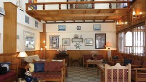 A cozy, well-lit living room with wooden furniture, a checkered floor, and a decorative wall with framed pictures and a ship's wheel. - Ionia (Skopelos)