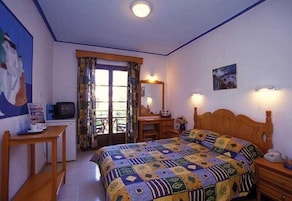 Un dormitorio con cama, escritorio, silla, televisor y ventana con cortinas.