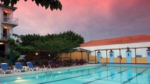 A swimming pool with lounge chairs and a covered area, surrounded by trees and buildings. - Ionia (Skopelos)