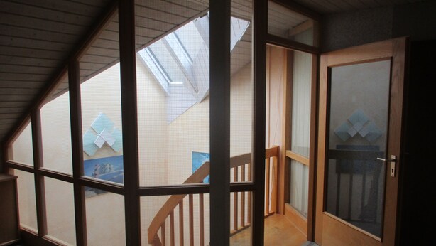 A room with a sloped ceiling, wooden beams, a skylight, a wooden staircase, and a sliding glass door. - Landhotel Lippach (Westhausen)