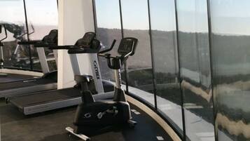 Un gimnasio con cintas de correr, elíptica y bicicleta estática, con amplias ventanas que ofrecen vistas del paisaje.