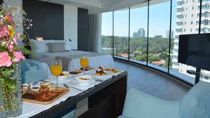 A modern hotel room with a large bed, a dining table with breakfast, a TV, and a city view. - Don Majestic Hotel Punta del Este (Punta del Este)