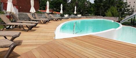 Un espace piscine avec une terrasse en bois, des chaises longues et des parasols.