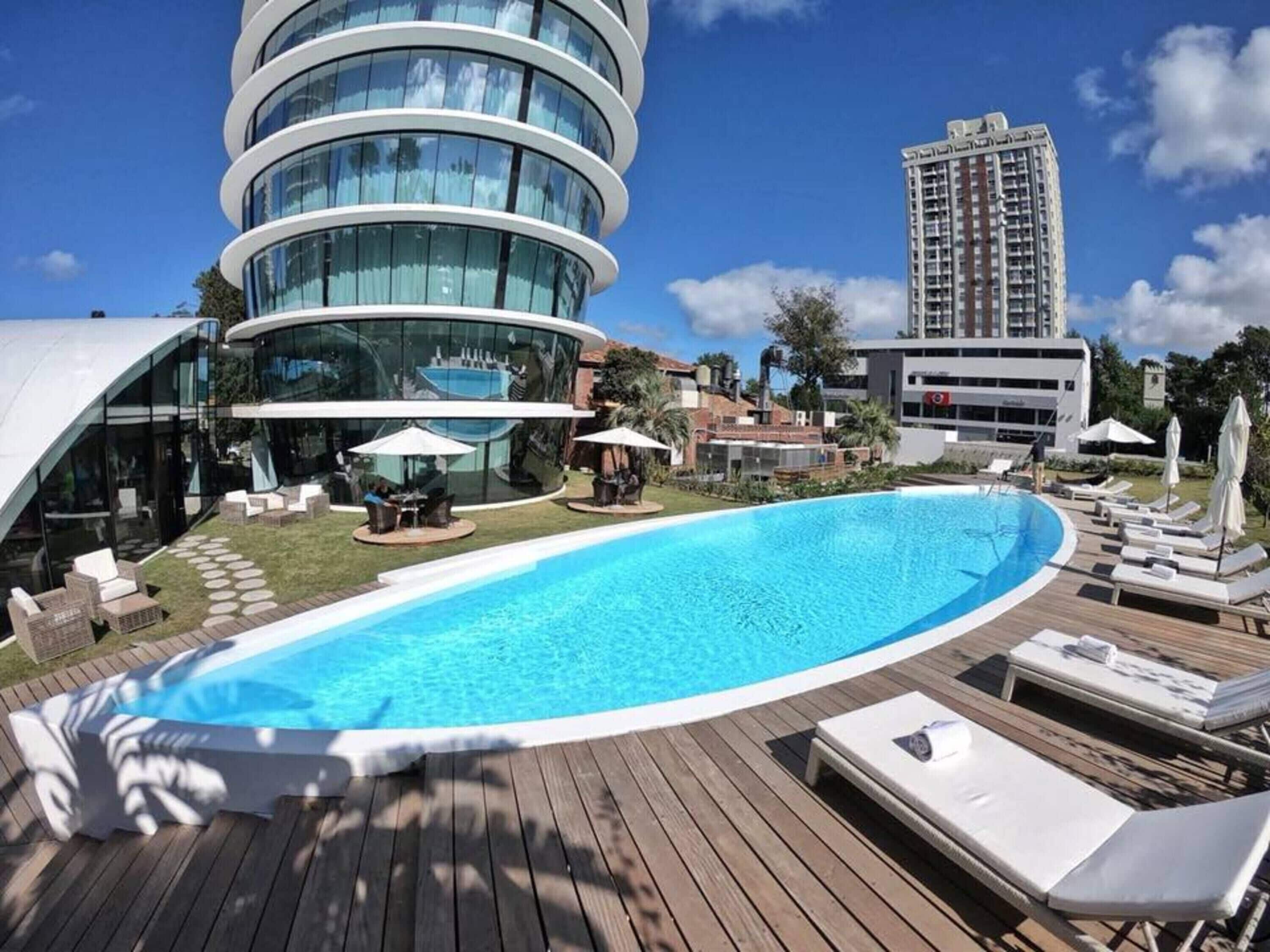 Un hotel moderno con un edificio circular de vidrio, una piscina y sillones de descanso.