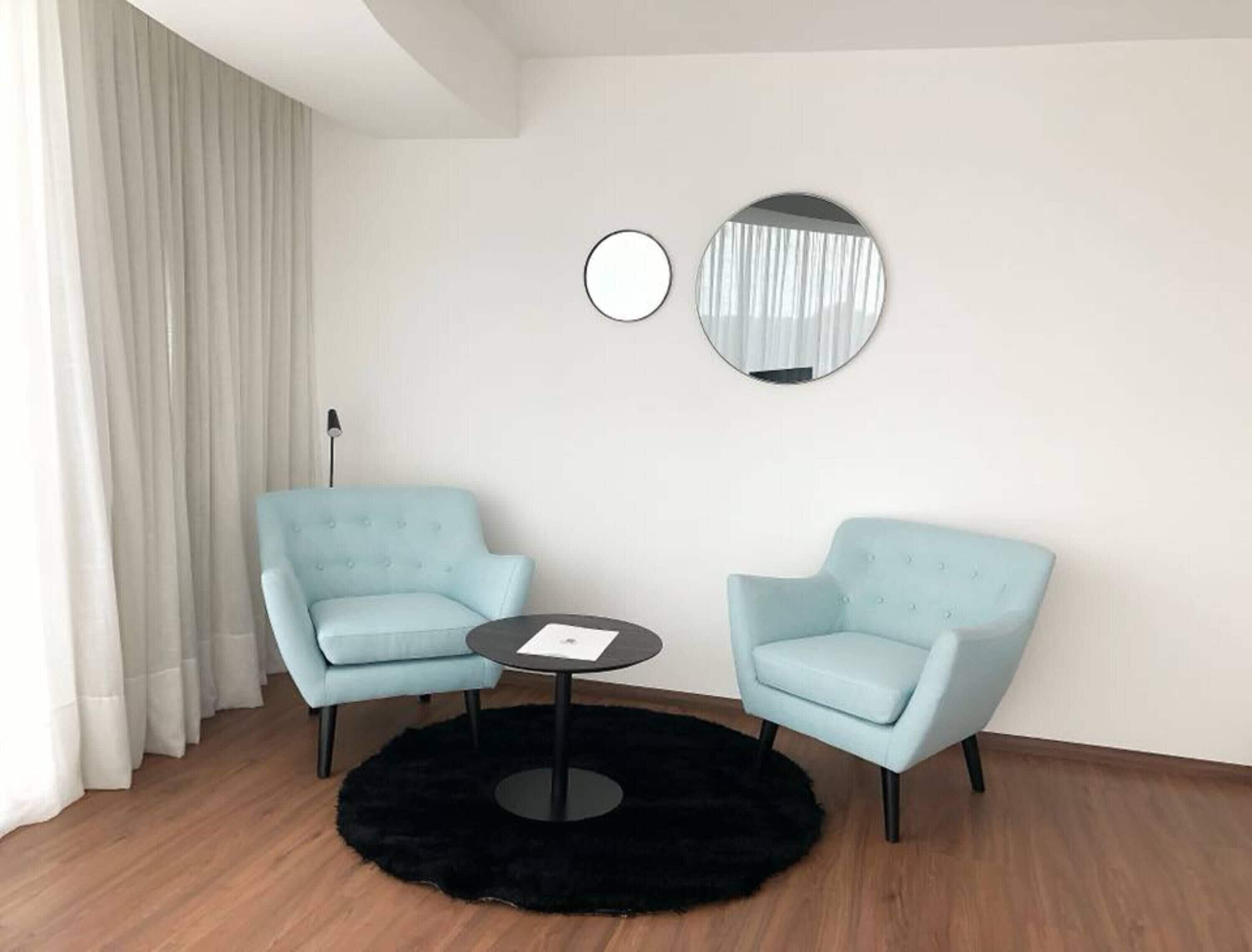 A room with two light blue armchairs, a small round table, and two wall-mounted mirrors.