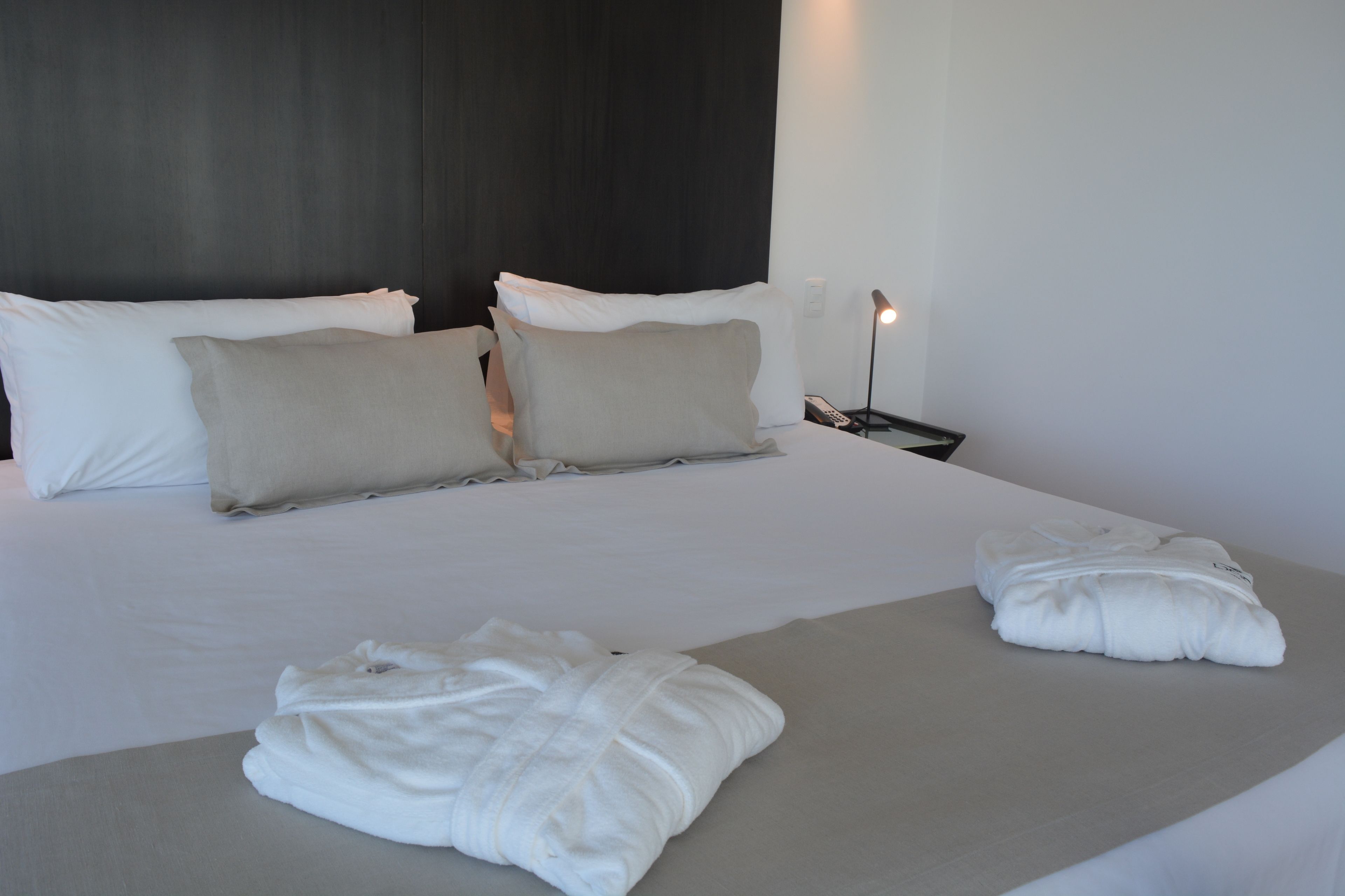 Una cama bien hecha con almohadas blancas y beige, una colcha gris y dos toallas blancas sobre la cama.