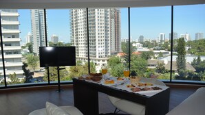A modern room with a dining table set for breakfast, a flat-screen TV, and a large window offering a city view. - Don Majestic Hotel Punta del Este (Punta del Este)