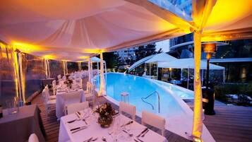 An outdoor dining area with tables set for a meal, a pool, and a covered seating area.