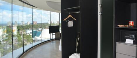 Una habitación de hotel moderna con un ventanal grande, un armario negro, un microondas y un refrigerador pequeño.