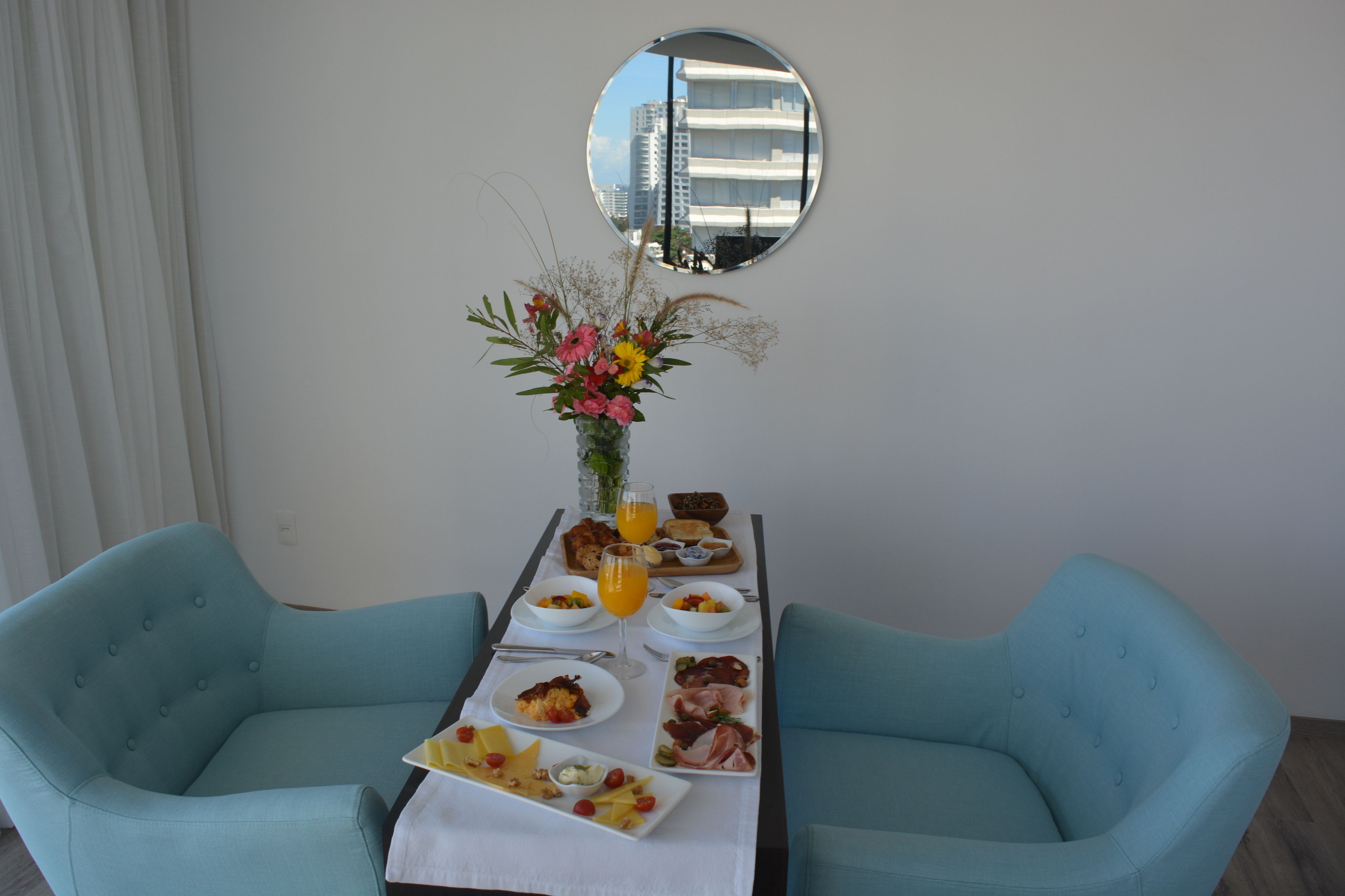 A dining table with breakfast items, a vase of flowers, and two blue chairs.