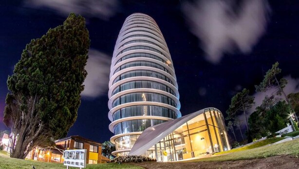 A modern building with a circular design, surrounded by trees and a well-maintained lawn. - Don Majestic Hotel Punta del Este (Punta del Este)