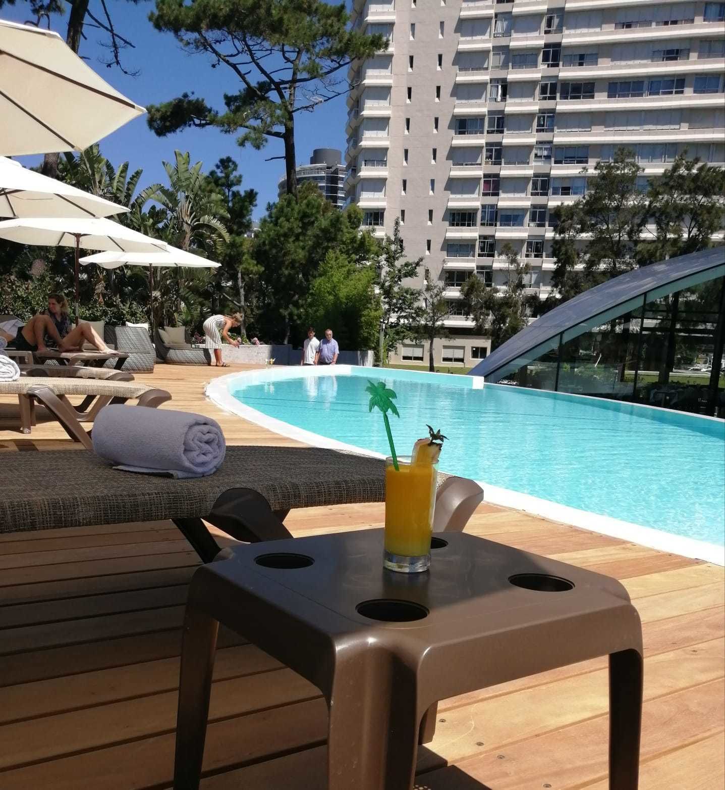 A poolside area with lounge chairs, umbrellas, and a drink on a table.