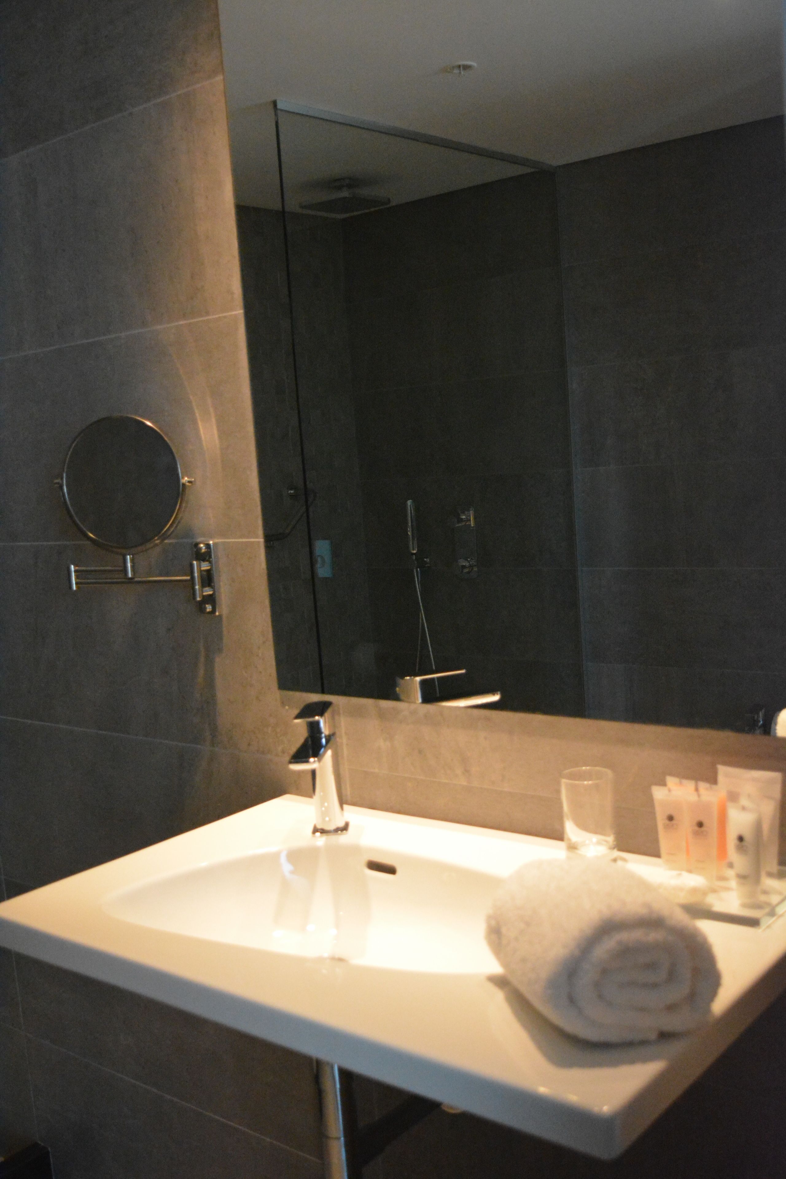 Un baño moderno con un lavamanos blanco, un espejo redondo y un vaso de agua.