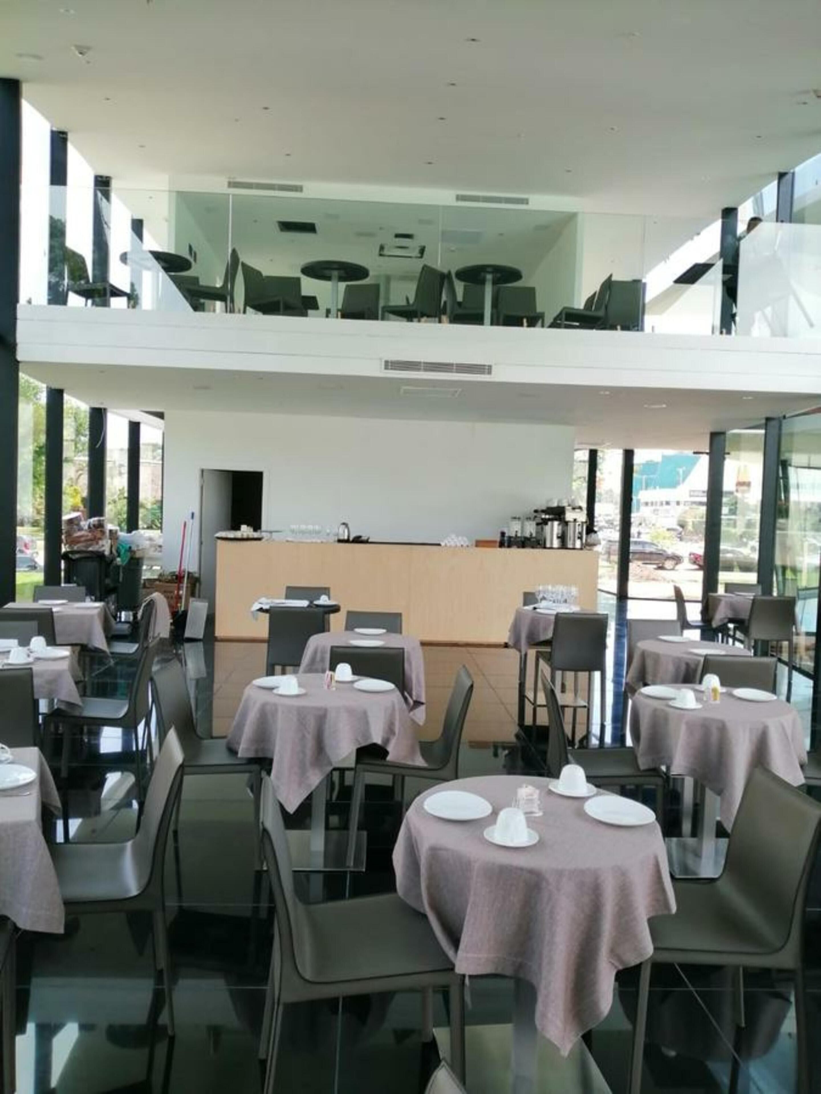 A modern dining area with glass tables and chairs, a central counter, and large windows offering a view of the outdoors.