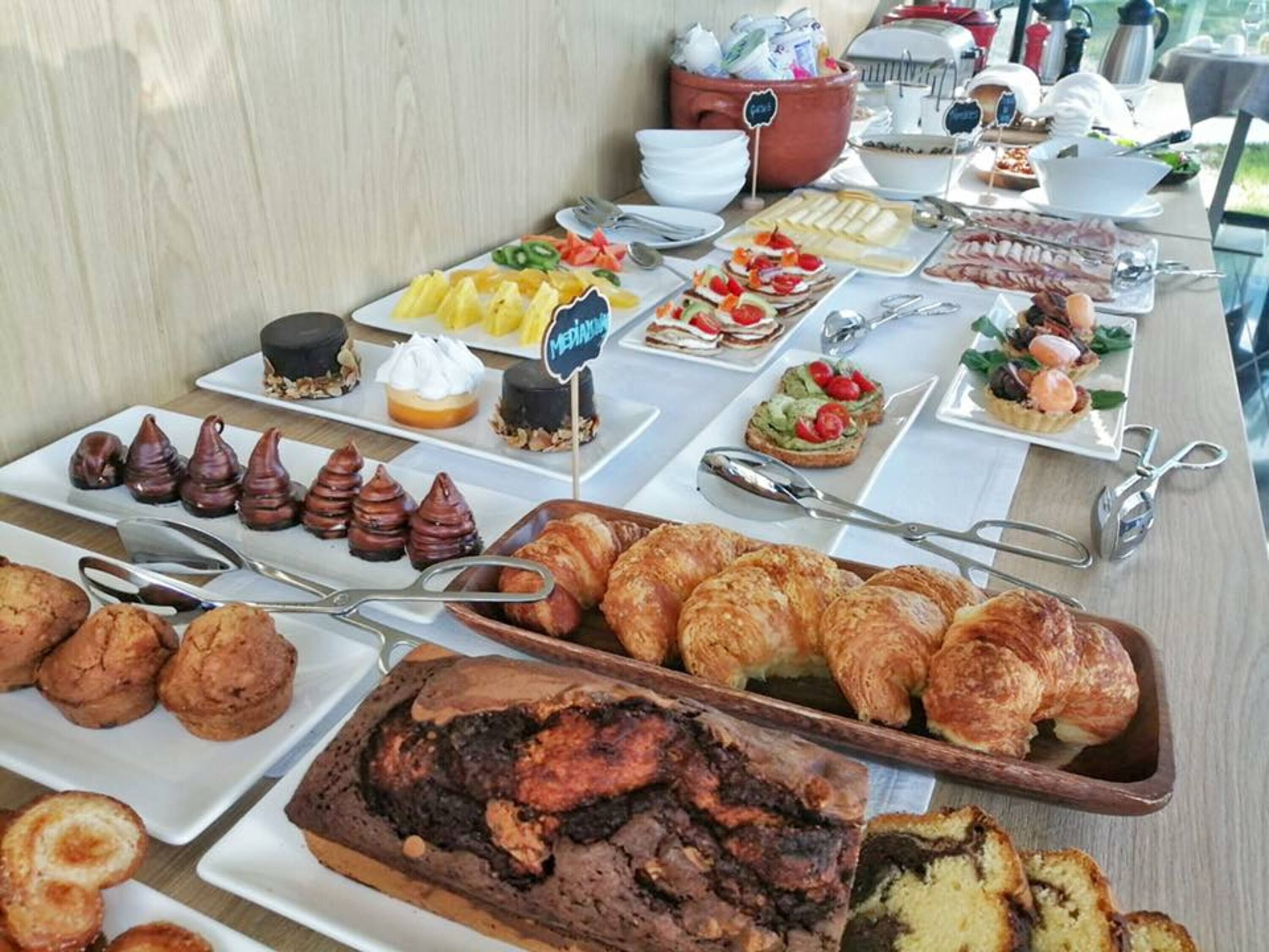Una mesa de buffet con diversos alimentos, incluyendo pasteles, postres y frutas.
