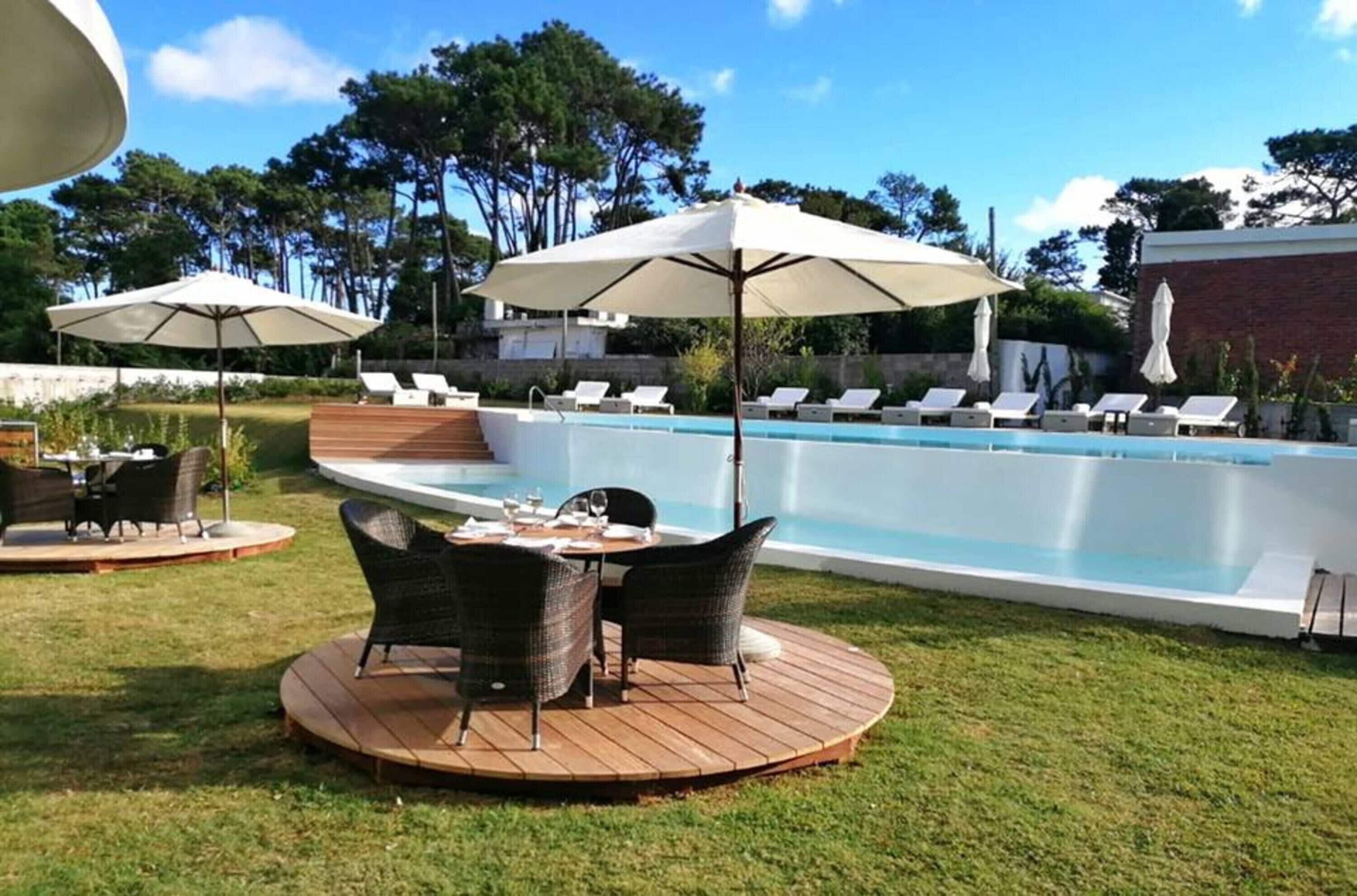Une piscine entourée d’une terrasse en bois et d’une pelouse, avec des chaises longues et des parasols à proximité.