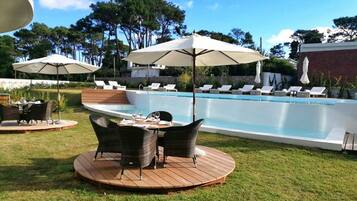 A swimming pool with lounge chairs and umbrellas, surrounded by a wooden deck and a grassy area.