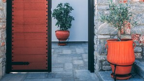 An arched stone doorway with a wooden door, a potted plant, and a wall-mounted light fixture. - Casa Di Bella (Volos)