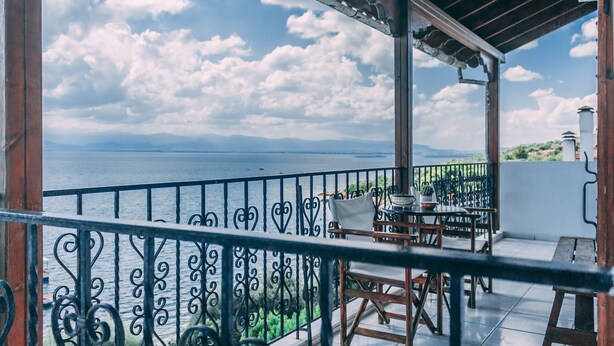 A balcony with a view of the sea, a table with chairs, and a railing. - Casa Di Bella (Volos)