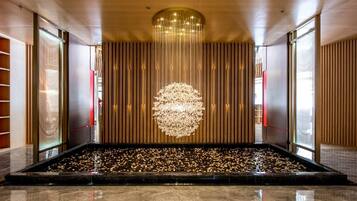 A spacious lobby with a reflective marble floor, a central water feature with floating pebbles, and a modern chandelier.