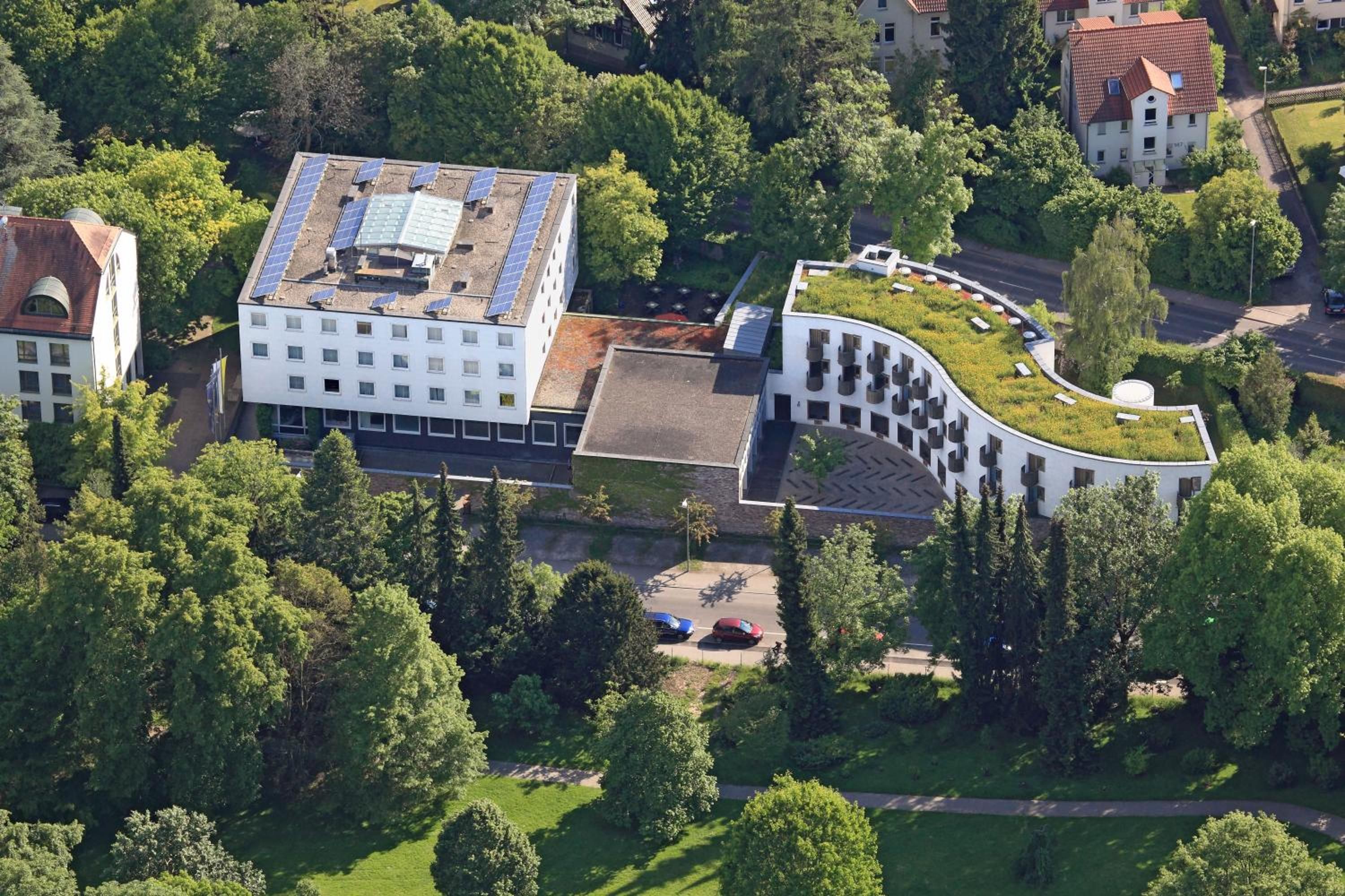 Un edificio con techo plano y paneles solares, rodeado de árboles y una estructura curva con techo verde.