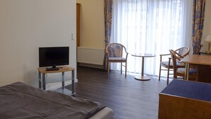 A hotel room with a bed, a TV on a stand, a small table, two chairs, a round table, and a window with curtains.