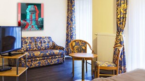 A hotel room with a sofa, a chair, a small table, a television, and a bed. - Hotel Restaurant Waldlust (Hagen)