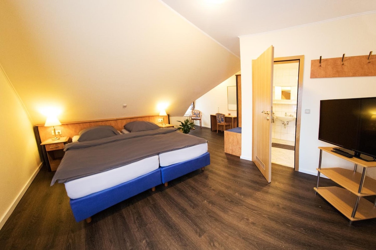 A bedroom with a bed, bedside tables, a TV, and a bathroom visible through an open door.