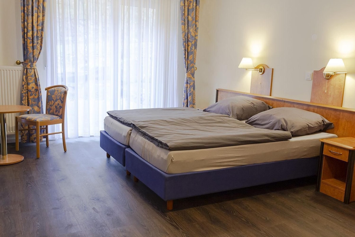 A hotel room with a bed, bedside tables, a chair, and a window with curtains.