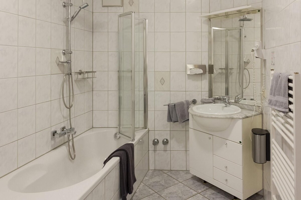 Un baño moderno con bañera, ducha con mampara de vidrio, lavabo y espejo.
