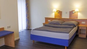 Un dormitorio con una cama, mesitas de noche, un escritorio y una ventana con cortinas.