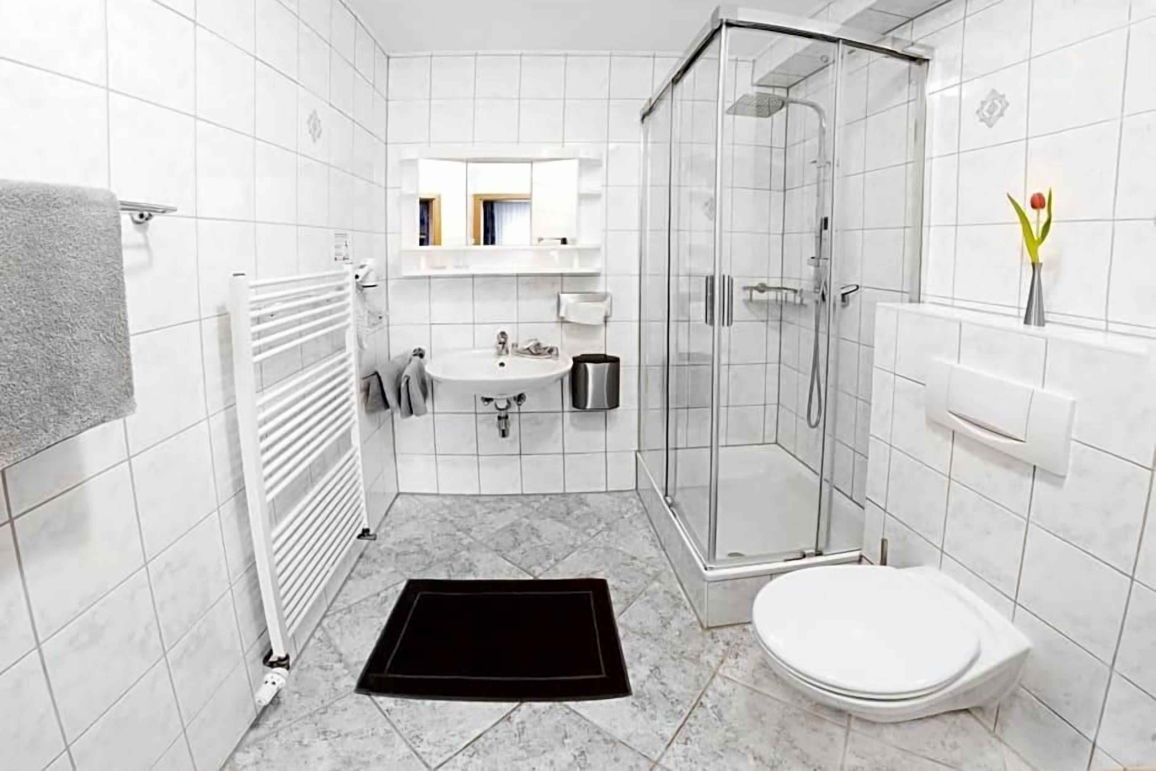 Un baño con lavamanos blanco, espejo, inodoro y ducha.