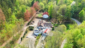 A large house with a red roof, surrounded by trees and a winding road.