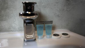 A bathroom sink with a chrome faucet, two tubes of shower gel, and two round soap containers.