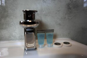 Un lavabo de salle de bain avec un robinet chromé, deux tubes de gel douche et deux distributeurs de savon ronds.