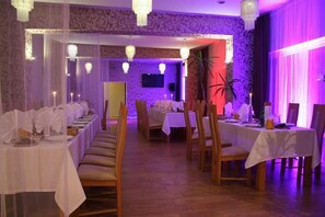A banquet hall with long tables set for a formal event, featuring chandeliers and draped curtains.