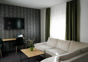 A modern living room with a flat-screen TV mounted on the wall, a sofa, a coffee table, and a desk with a chair.