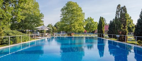 Piscina azul cristalina rodeada por árvores e uma área coberta com espreguiçadeiras.