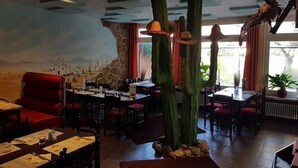 A restaurant interior with high ceilings, stone walls, and a mural. Tables are set with menus and cutlery. - Desperados Hotel (Bergen)