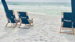 Drei Strandstühle mit 'Sandestin'-Branding auf einem Sandstrand mit Blick aufs Meer.