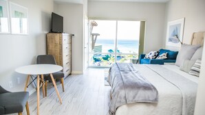 Ein modernes Hotelzimmer mit Bett, Schreibtisch und Stuhl. Durch das Fenster ist der Strand zu sehen.